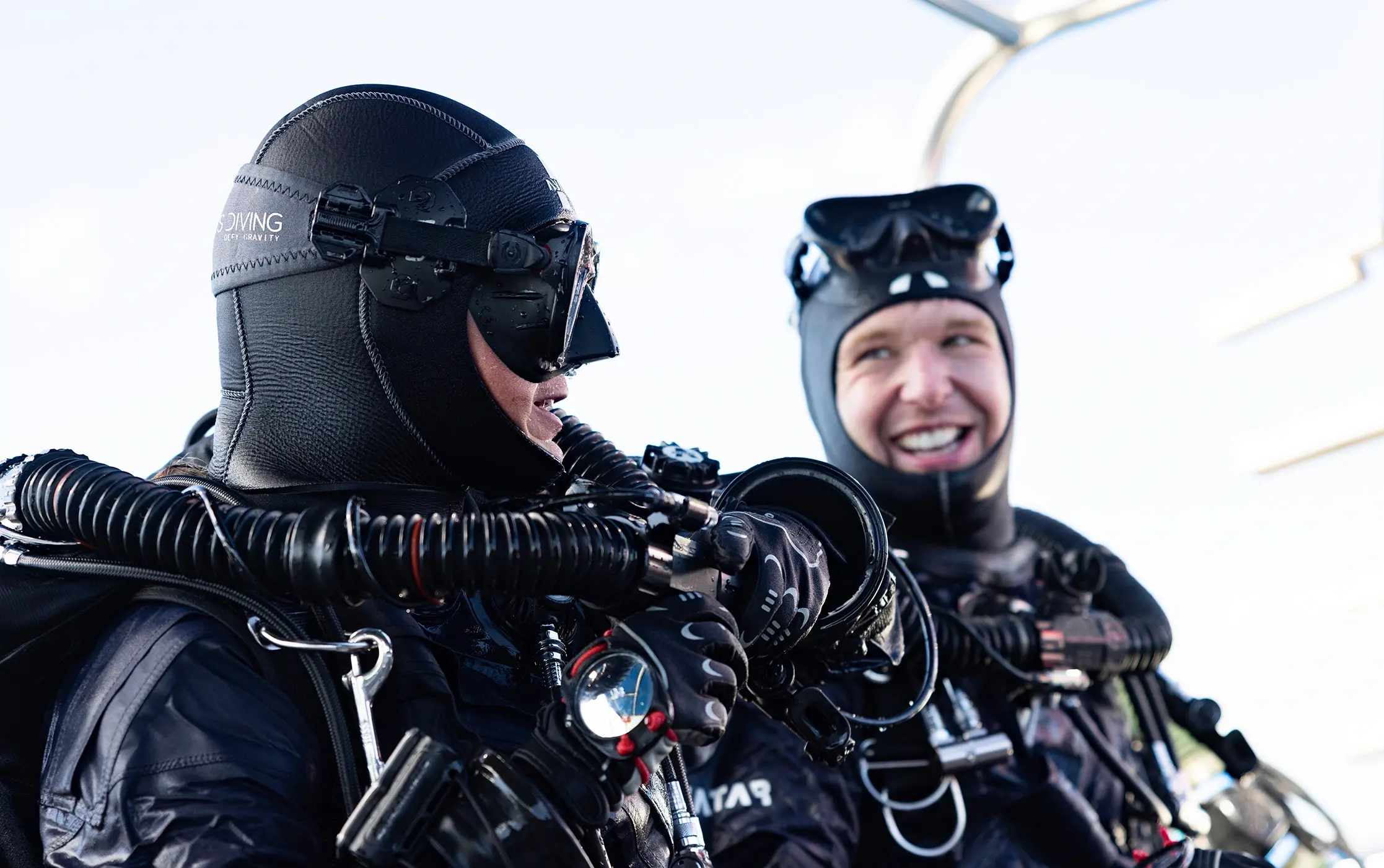 Two divers with diving equipment just after a dive, talking and smiling, one looking at the other